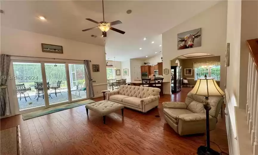 Living room with a wealth of natural light, dark wood-type flooring, high vaulted ceiling, and ceiling fan with notable chandelier