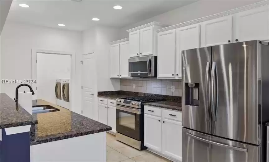 Kitchen featuring backsplash, independent washer and dryer, appliances with stainless steel finishes, sink, and white cabinetry