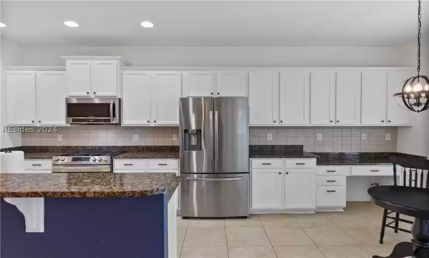 Kitchen featuring white cabinetry, a breakfast bar, decorative light fixtures, backsplash, and stainless steel appliances