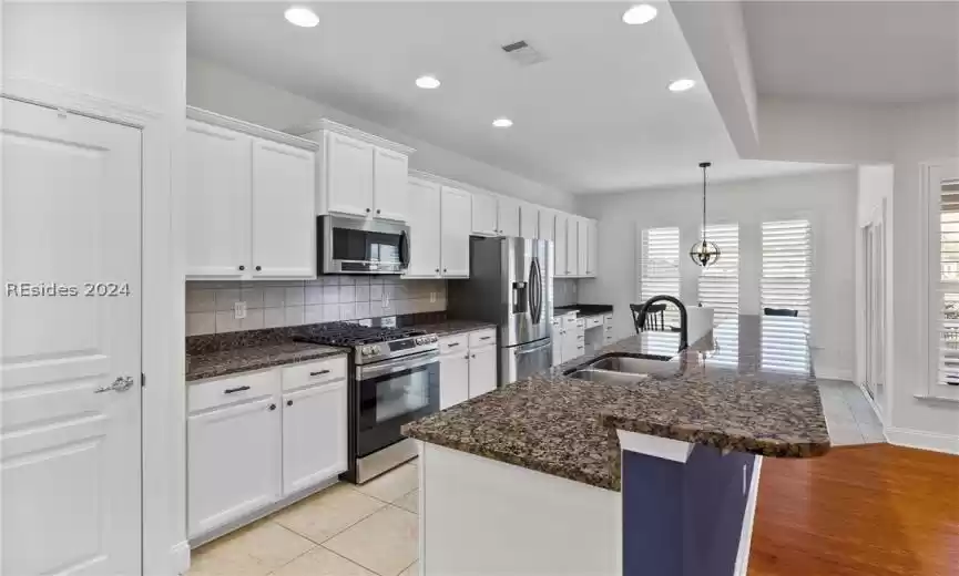 Kitchen with sink, an island with sink, backsplash, light hardwood / wood-style floors, and stainless steel appliances