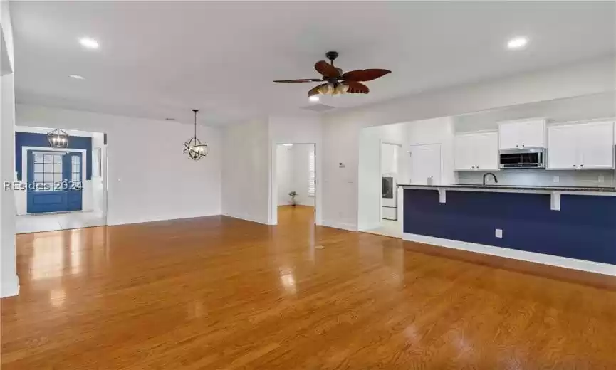 Unfurnished living room with ceiling fan with notable chandelier, sink, and light hardwood / wood-style floors