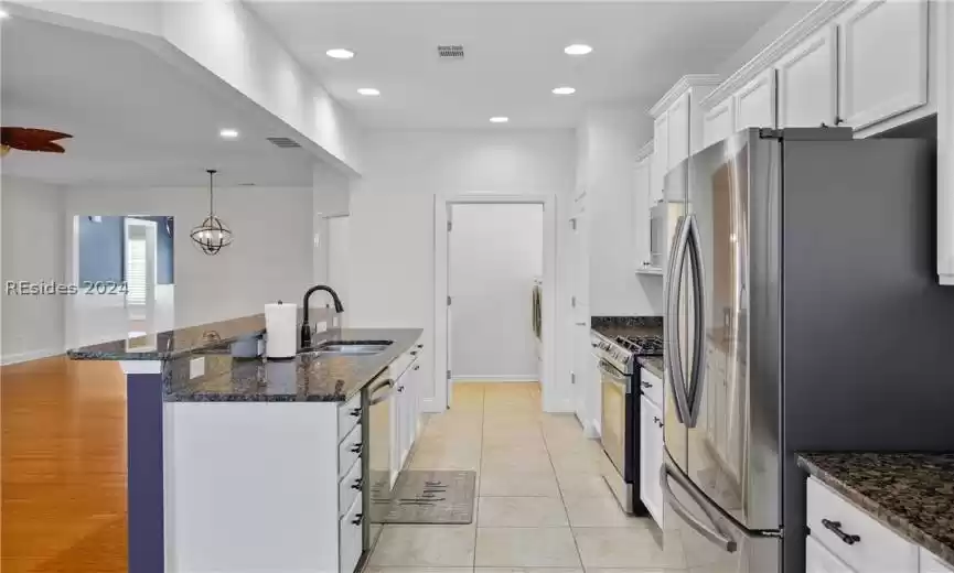 Kitchen with sink, white cabinets, pendant lighting, light tile floors, and appliances with stainless steel finishes