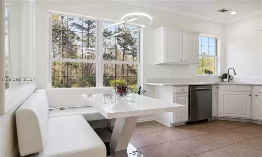 Kitchen featuring white cabinets, light tile floors, stainless steel dishwasher, crown molding, and sink
