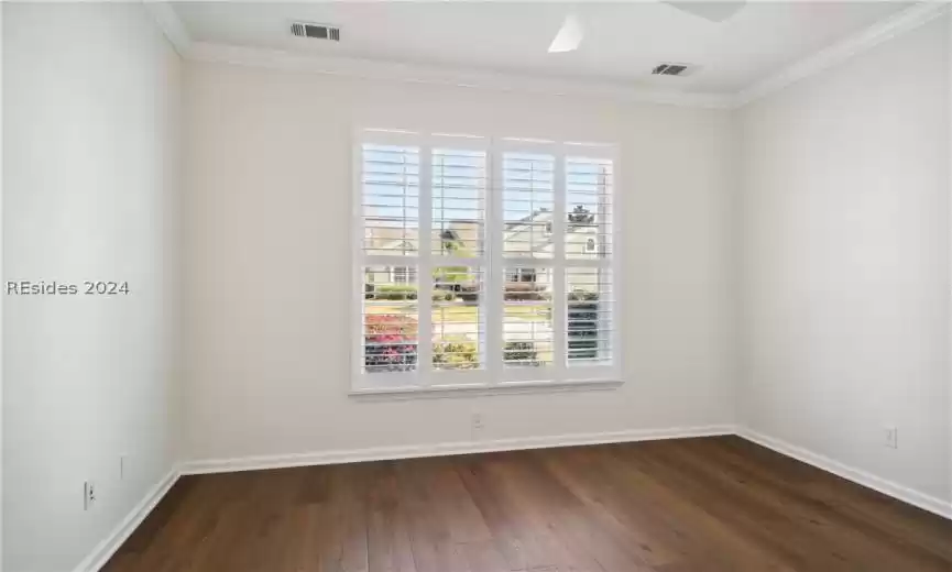 Empty room with dark wood-type flooring, crown molding, and ceiling fan
