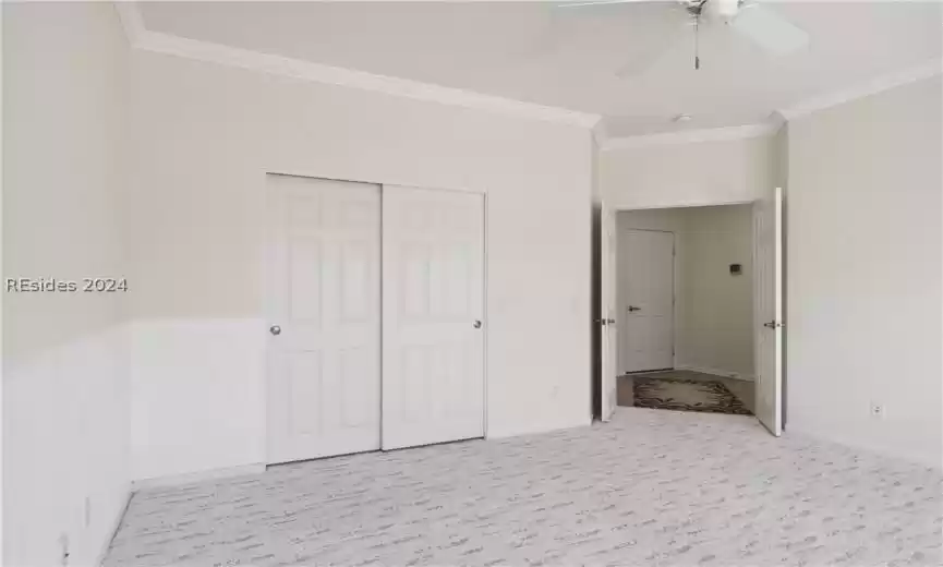 Unfurnished bedroom featuring light carpet, a closet, crown molding, and ceiling fan