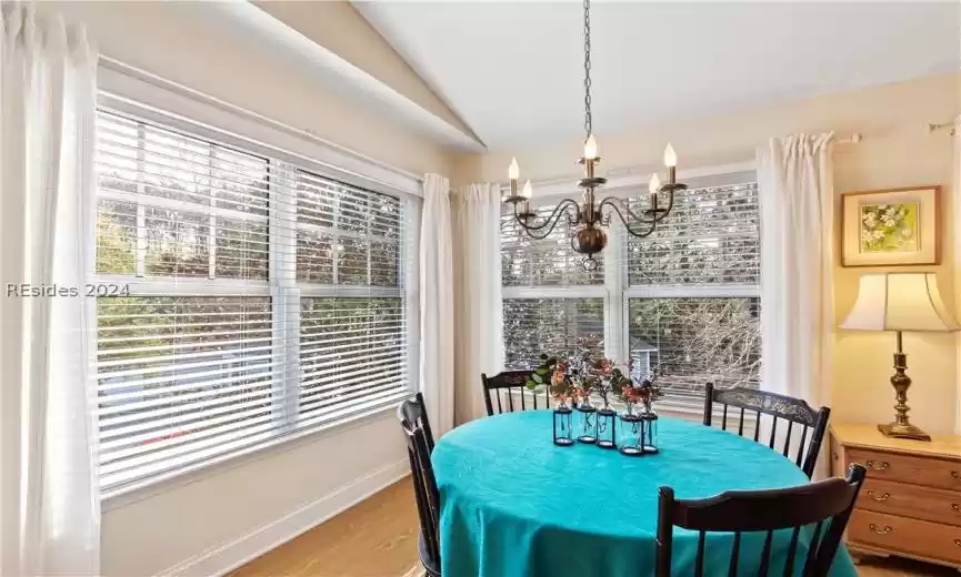 Dining room with an inviting chandelier, light hardwood / wood-style flooring, and vaulted ceiling,. Blinds, insulated shades, and curtains.
