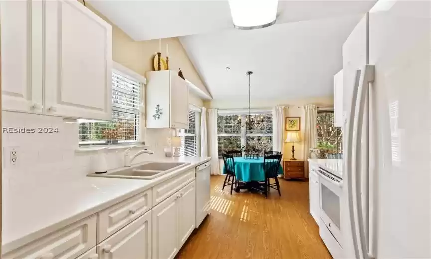 Kitchen featuring white appliances, vaulted ceiling, light wood-type flooring, backsplash, and white cabinetry