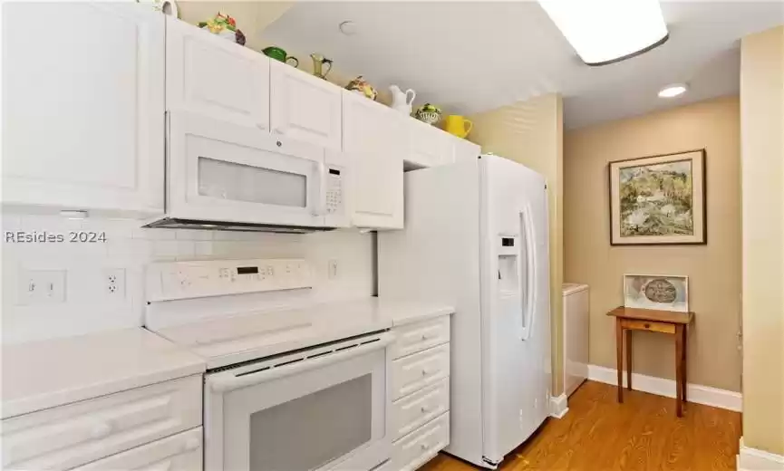 Kitchen with white cabinetry, white appliances, light hardwood / wood-style flooring, and backsplash