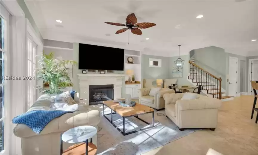 Living room with built in shelves, crown molding, and ceiling fan with beautiful Stone floors