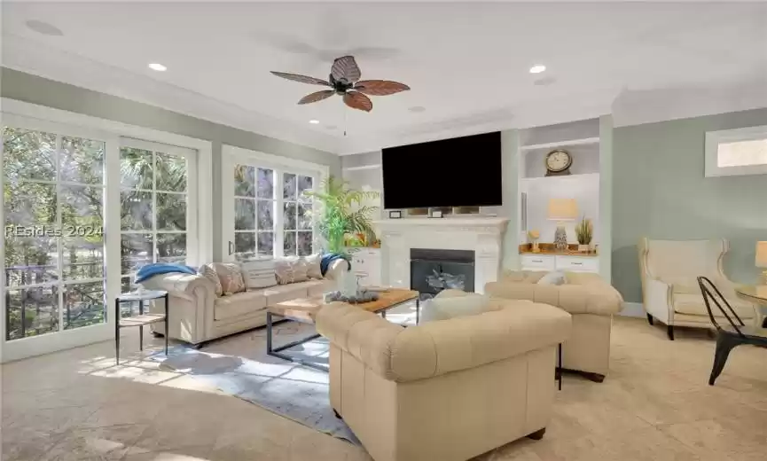Living room with ceiling fan, built in shelves, crown molding, and a wealth of natural light