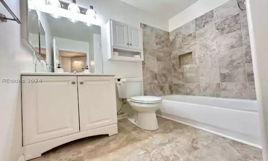 Full bathroom with tiled shower / bath, toilet, tile floors, and oversized vanity