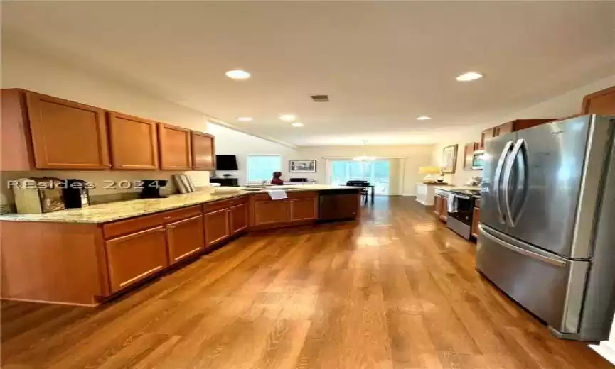 Kitchen featuring decorative light fixtures, a notable chandelier, appliances with stainless steel finishes, light hardwood / wood-style floors, and light stone counters