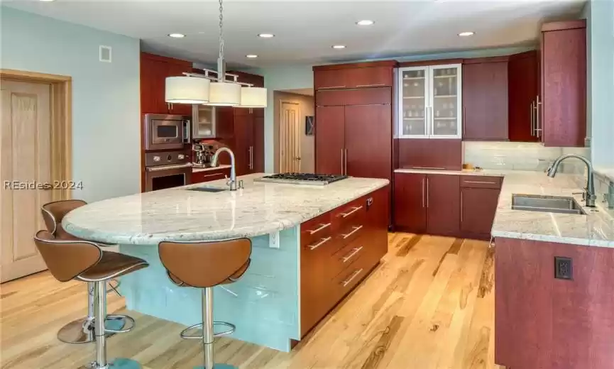 Kitchen featuring built in appliances, a kitchen island with sink, sink, and light wood-type flooring