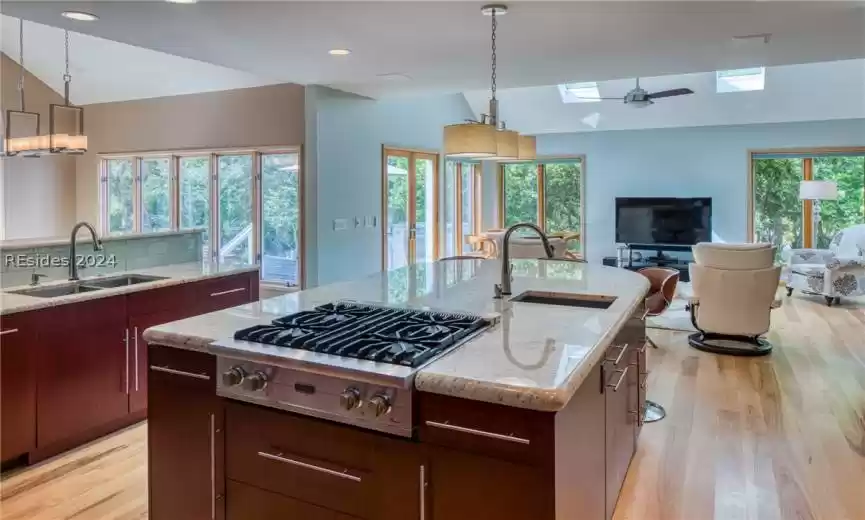 Kitchen with an island with sink, pendant lighting, ceiling fan, a healthy amount of sunlight, and light wood-type flooring