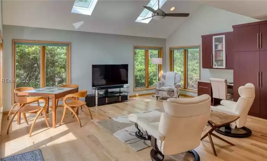 Living room featuring a skylight, high vaulted ceiling, light hardwood / wood-style floors, and ceiling fan