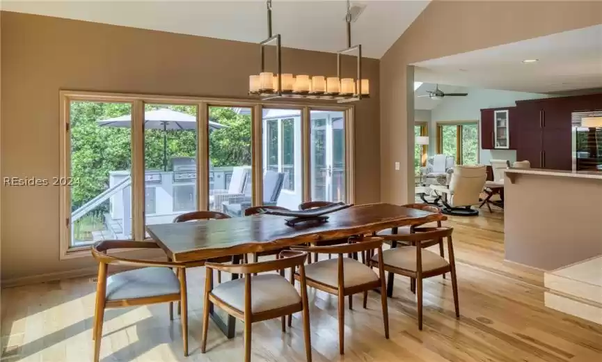 Dining area with high vaulted ceiling, ceiling fan with notable chandelier, and light hardwood / wood-style flooring