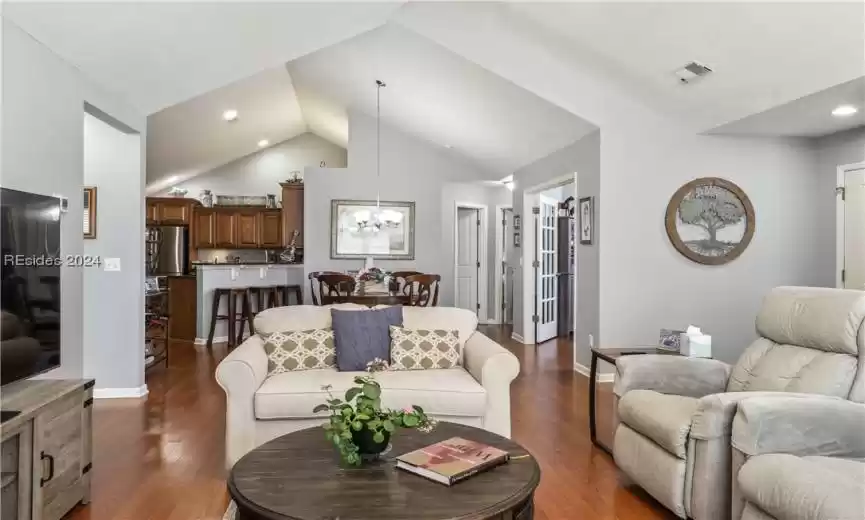 Living room featuring an inviting chandelier, vaulted ceiling, and dark hardwood / wood-style floors