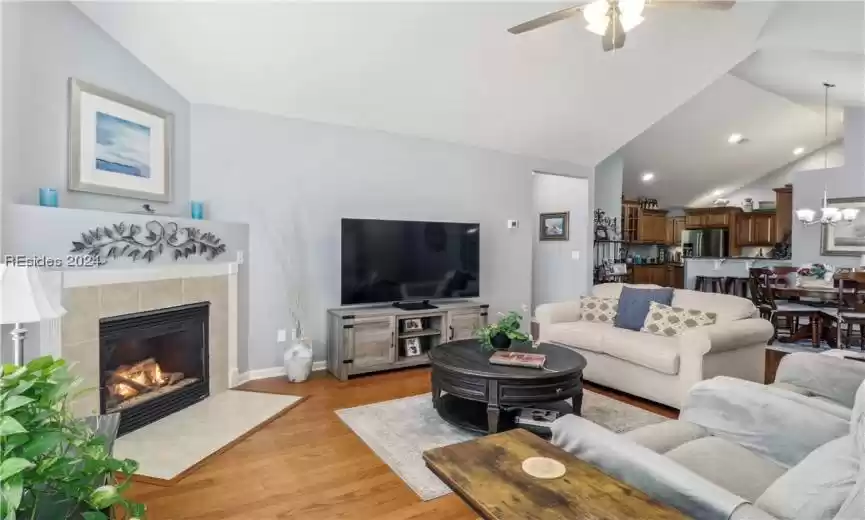 Living room with ceiling fan with notable chandelier, light hardwood / wood-style flooring, lofted ceiling, and a tiled fireplace