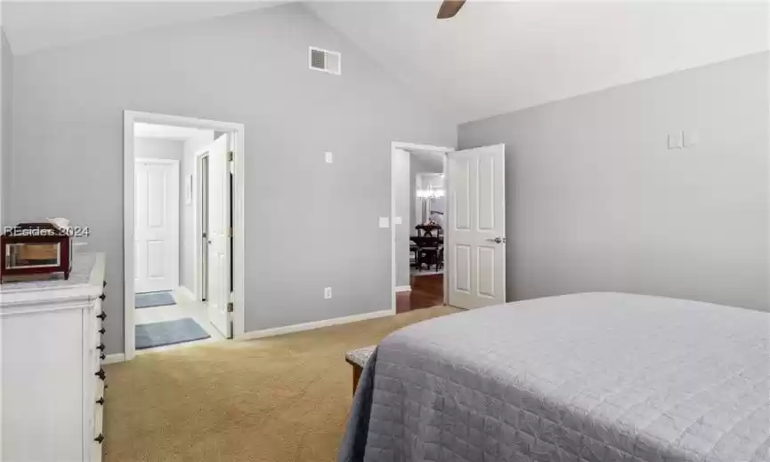 Carpeted bedroom with ceiling fan with notable chandelier, high vaulted ceiling, and connected bathroom