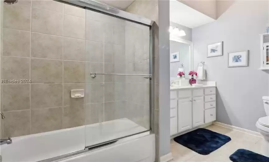 Full bathroom with tile flooring, bath / shower combo with glass door, toilet, and vanity