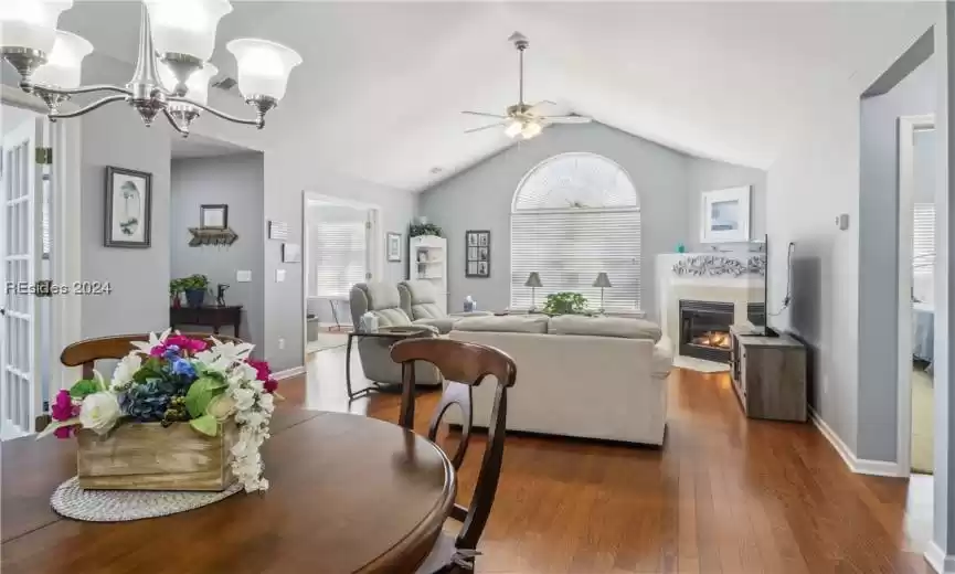 Dining room with ceiling fan with notable chandelier, vaulted ceiling, plenty of natural light, and dark hardwood / wood-style floors