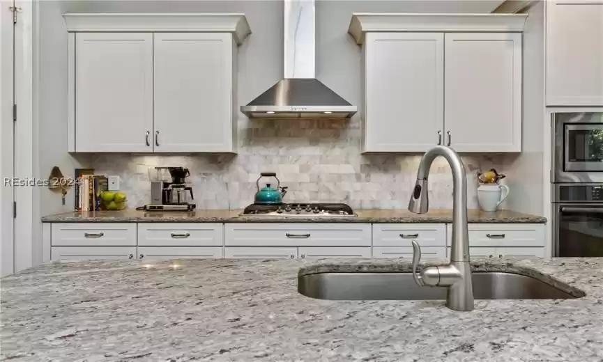 Kitchen with white cabinets, appliances with stainless steel finishes, tasteful backsplash, and wall chimney range hood