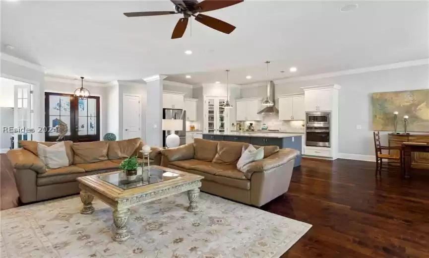 Living room with crown molding, french doors, ceiling fan with notable chandelier, and dark wood-type flooring