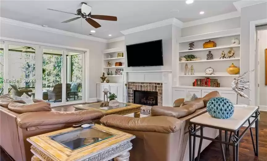 Living room with crown molding, ceiling fan, dark wood-type flooring, and a fireplace