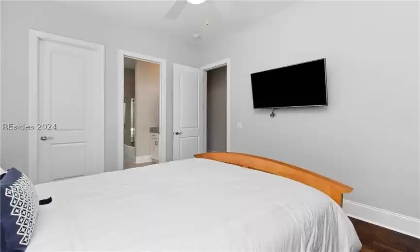 Bedroom with dark hardwood / wood-style floors, ceiling fan, and ensuite bath