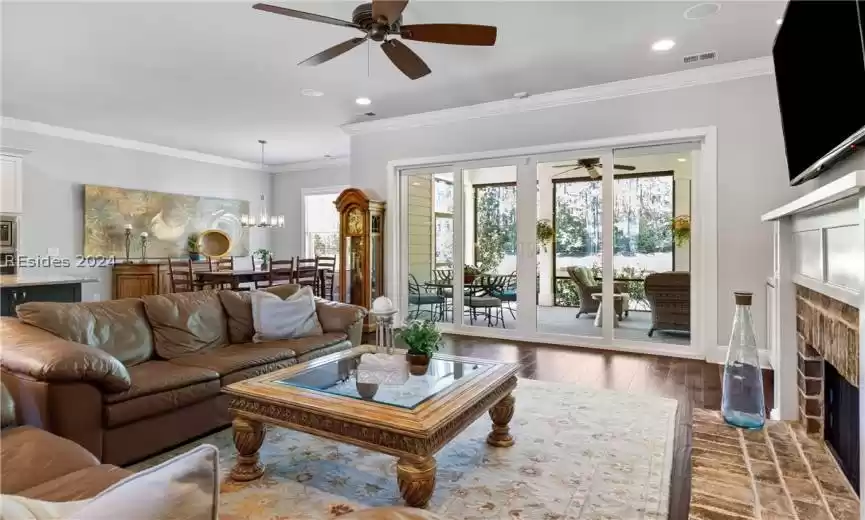 Living room featuring ornamental molding, a brick fireplace, dark hardwood / wood-style floors, and ceiling fan with notable chandelier