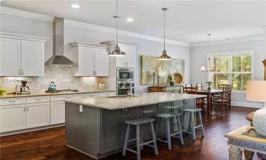 Kitchen featuring a center island with sink, hanging light fixtures, wall chimney exhaust hood, and dark hardwood / wood-style flooring