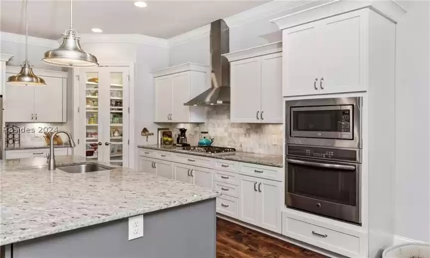 Kitchen featuring dark hardwood / wood-style floors, wall chimney exhaust hood, sink, stainless steel appliances, and tasteful backsplash