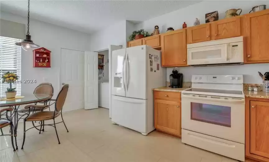 Kitchen featuring light tile flooring, hanging light fixtures, appliances, and a textured ceiling