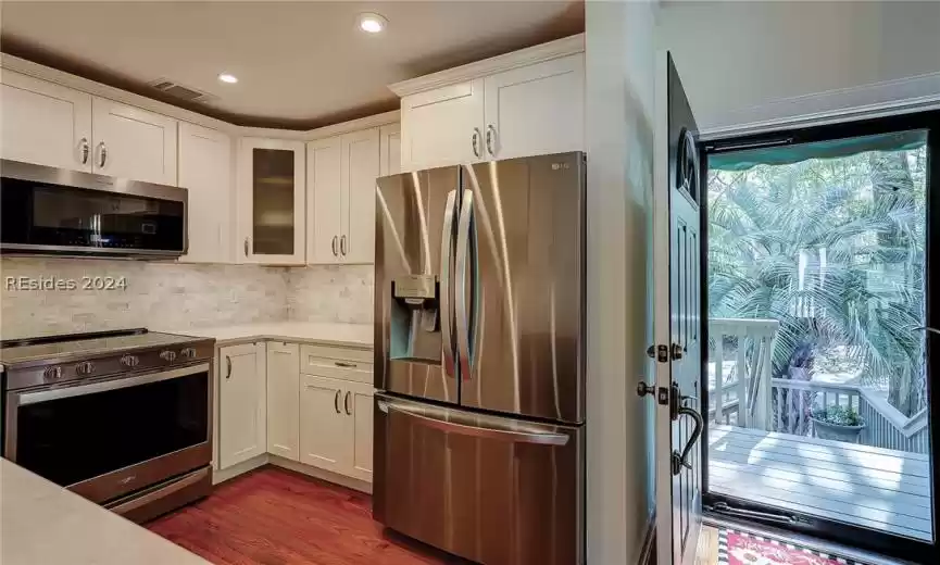 Kitchen with dark hardwood / wood-style flooring, stainless steel appliances, white cabinets, and tasteful backsplash