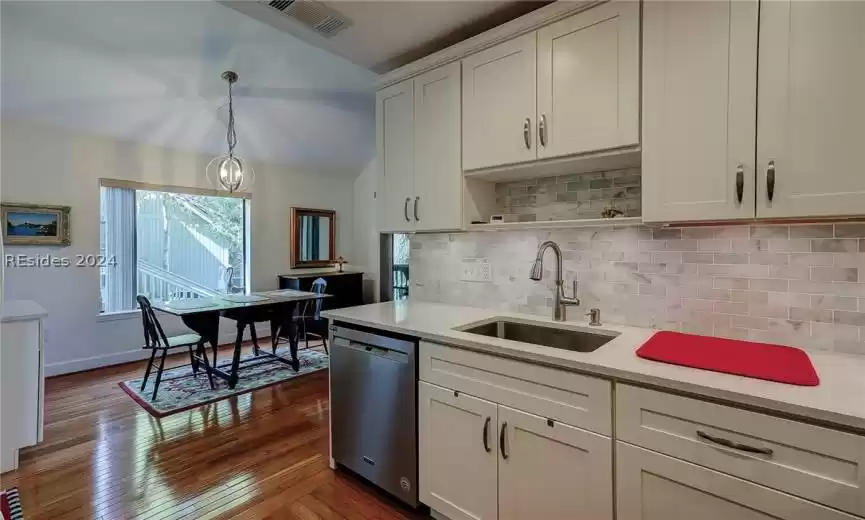 Kitchen with backsplash, white cabinets, sink, dishwasher, and hanging light fixtures