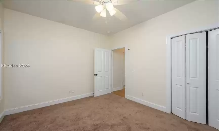 Unfurnished bedroom featuring a closet, light carpet, and ceiling fan