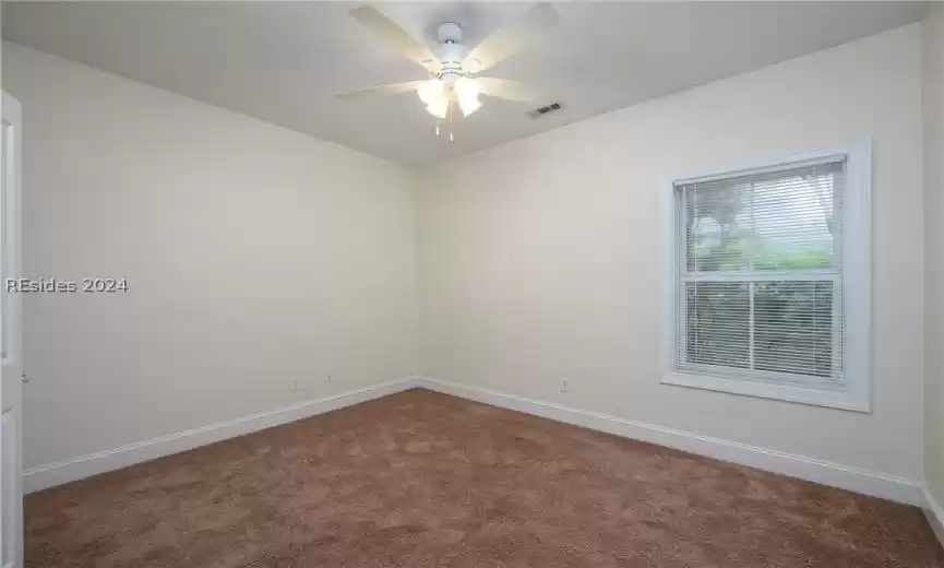 Spare room featuring ceiling fan and dark colored carpet