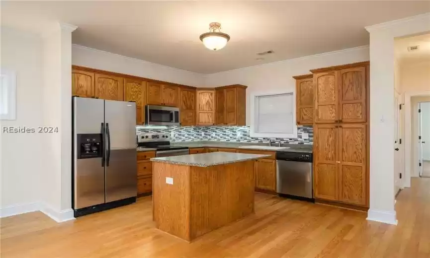 Kitchen with a kitchen island, tasteful backsplash, ornamental molding, appliances with stainless steel finishes, and light wood-type flooring