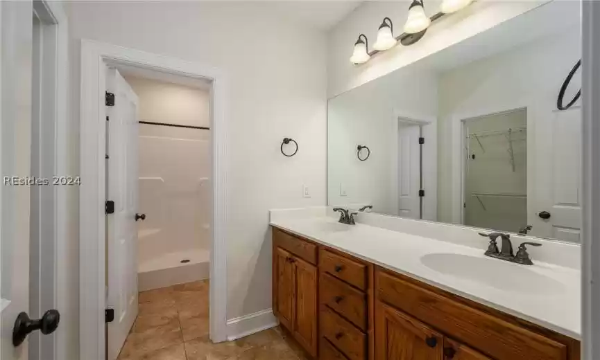 Bathroom with dual sinks, a shower, tile floors, and vanity with extensive cabinet space