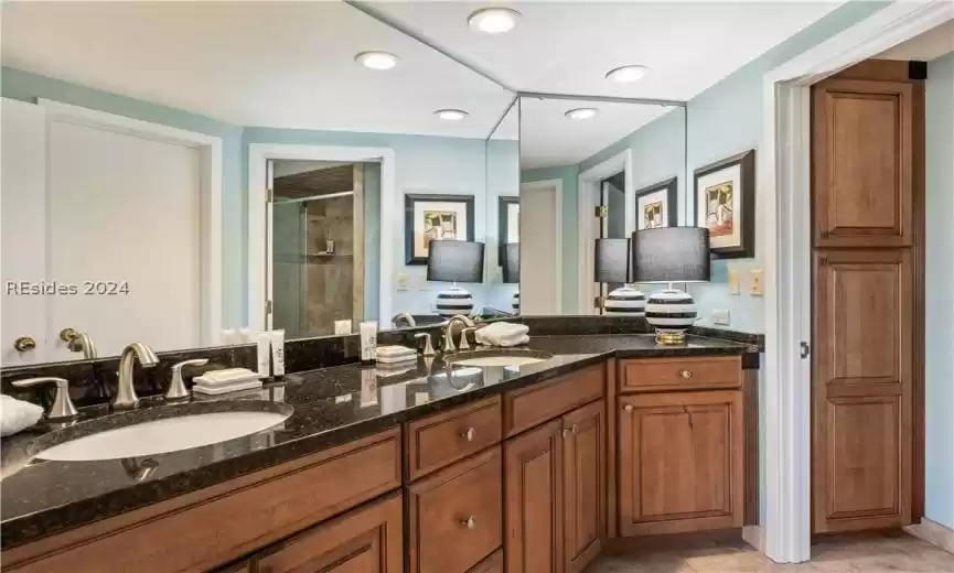 Spacious primary bathroom with granite countertop, dual vanity, and wood cabinetry.