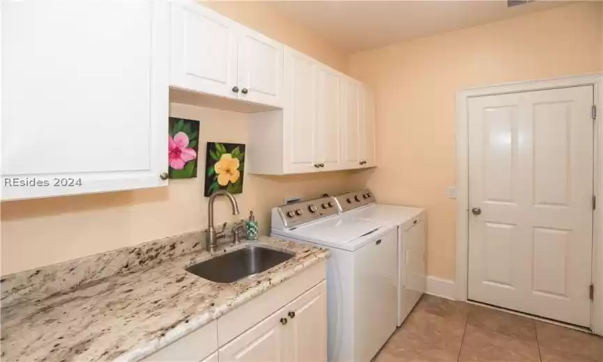 Clothes washing area with washing machine and dryer, sink, cabinets, drop-down ironing board, granite countertop, stainless steel utility sink and light tile flooring