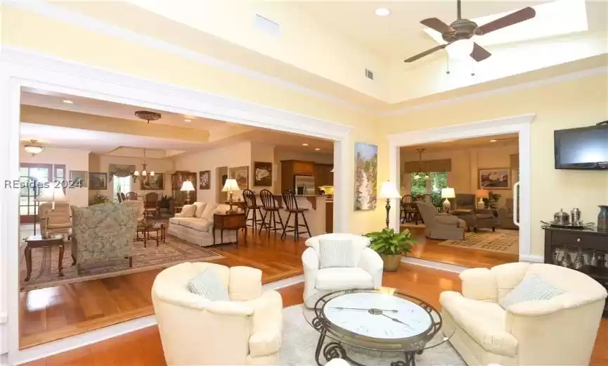 Living room featuring wood-type flooring, ceiling fan with notable chandelier, a high ceiling, and a healthy amount of sunlight