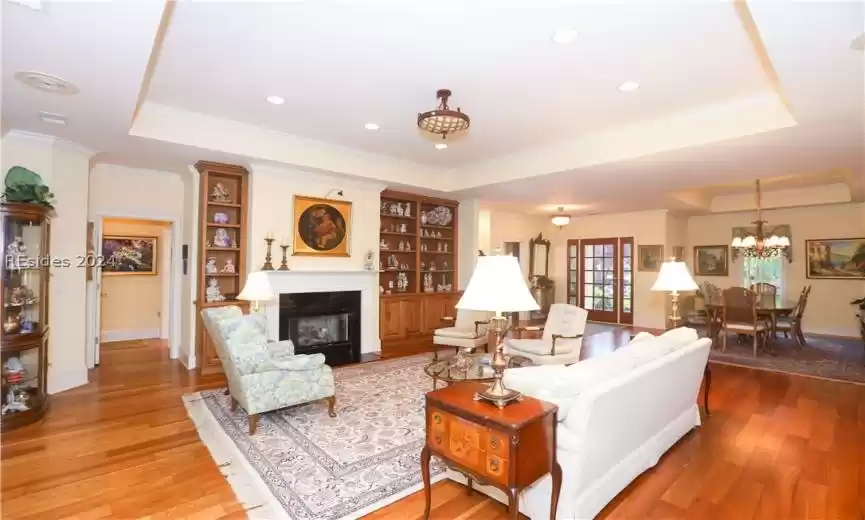 Living room with an inviting chandelier, ornamental molding, a tray ceiling, and hardwood / wood-style flooring