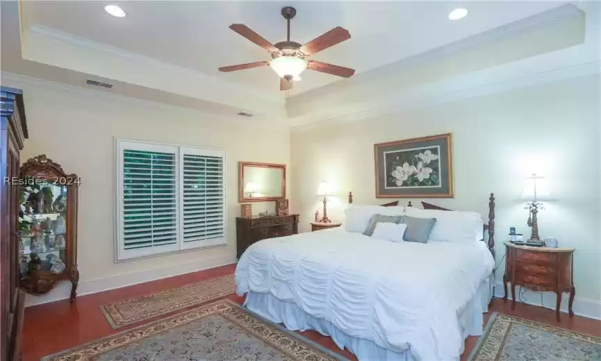 Bedroom with a tray ceiling, ceiling fan, dark wood-type flooring, and crown molding