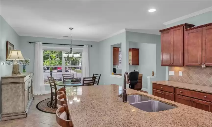 Kitchen with hanging light fixtures, light tile flooring, tasteful backsplash, light stone counters, and an inviting chandelier