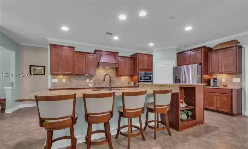 Kitchen featuring a kitchen breakfast bar, custom exhaust hood, stainless steel appliances, and a center island with sink