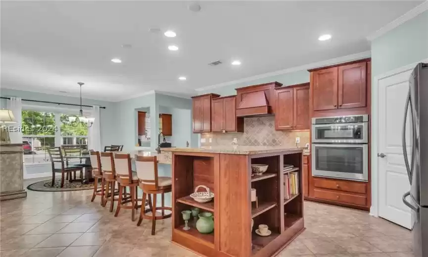 Kitchen with pendant lighting, custom range hood, stainless steel appliances, and light tile floors