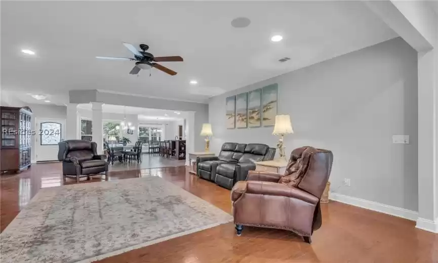 Living room with hardwood / wood-style floors, ceiling fan with notable chandelier, and decorative columns