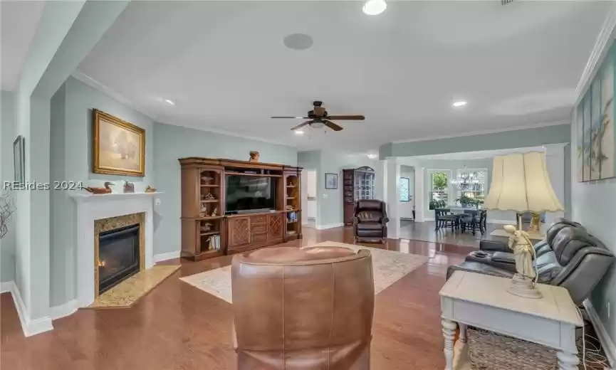 Living room with ornamental molding, ceiling fan, and dark wood-type flooring