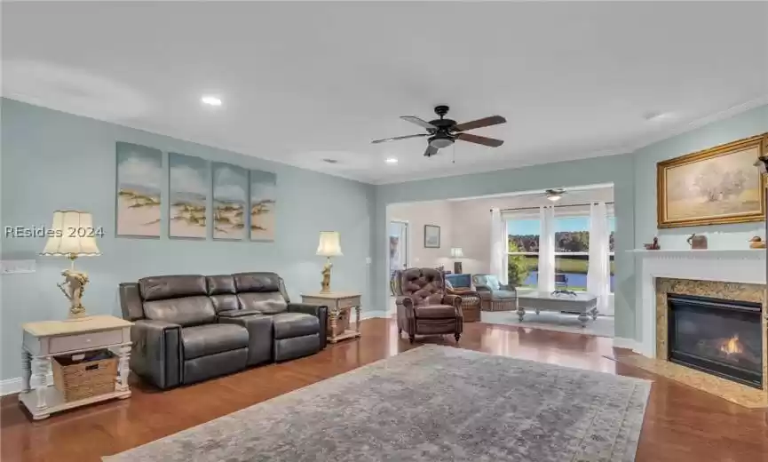 Living room with ornamental molding, ceiling fan, a fireplace, and dark hardwood / wood-style floors